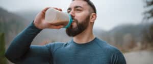 A man drinks a protein shake out of a bottle outside