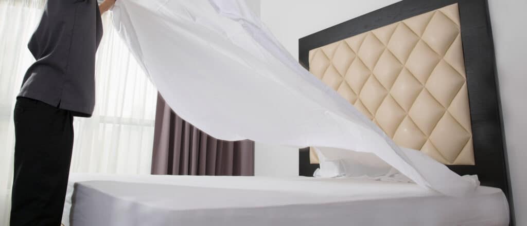 A man floats a clean white sheet over his bed
