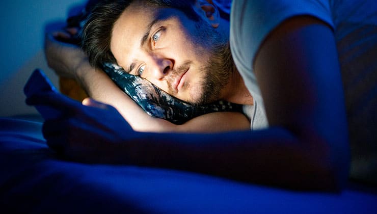 A man looks at his phone in bed