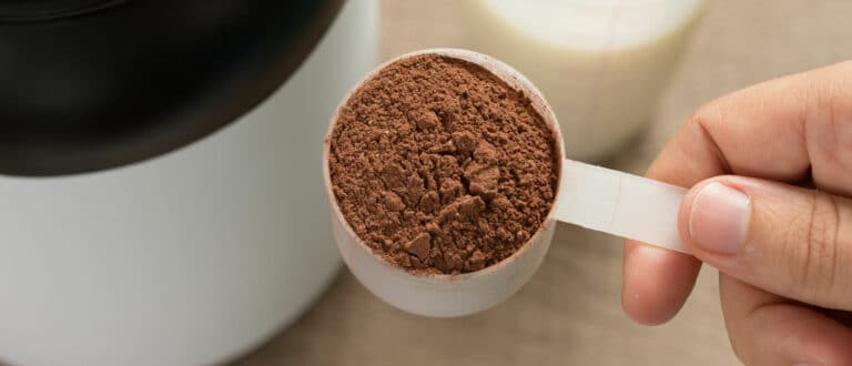 Close up of a man holding a scoop of chocolate protein powder