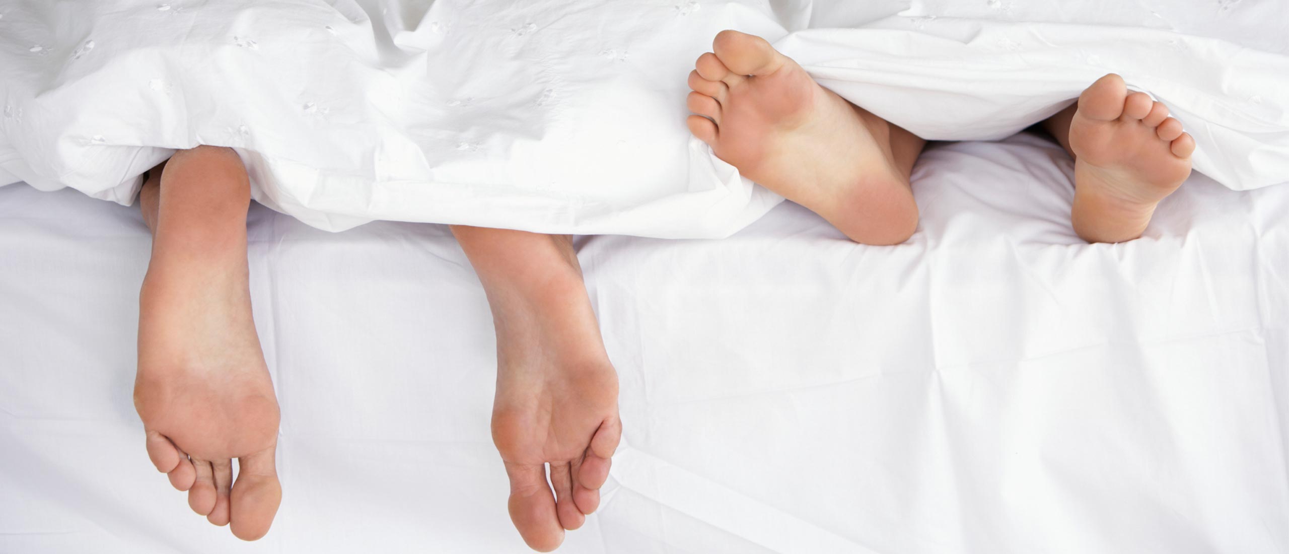 Male and female feet in bed under the blankets