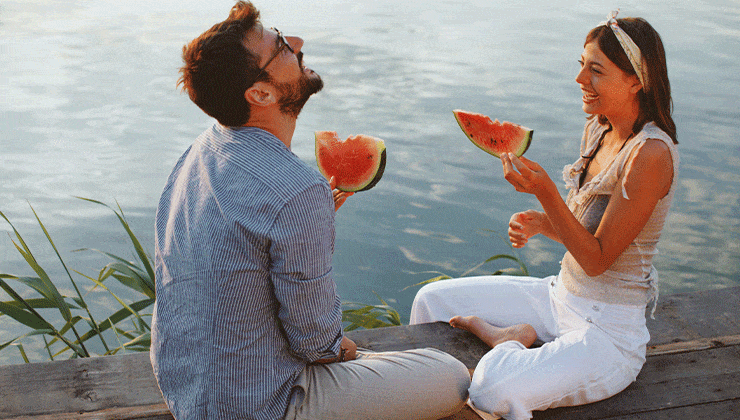 man and woman eating watermelon by water