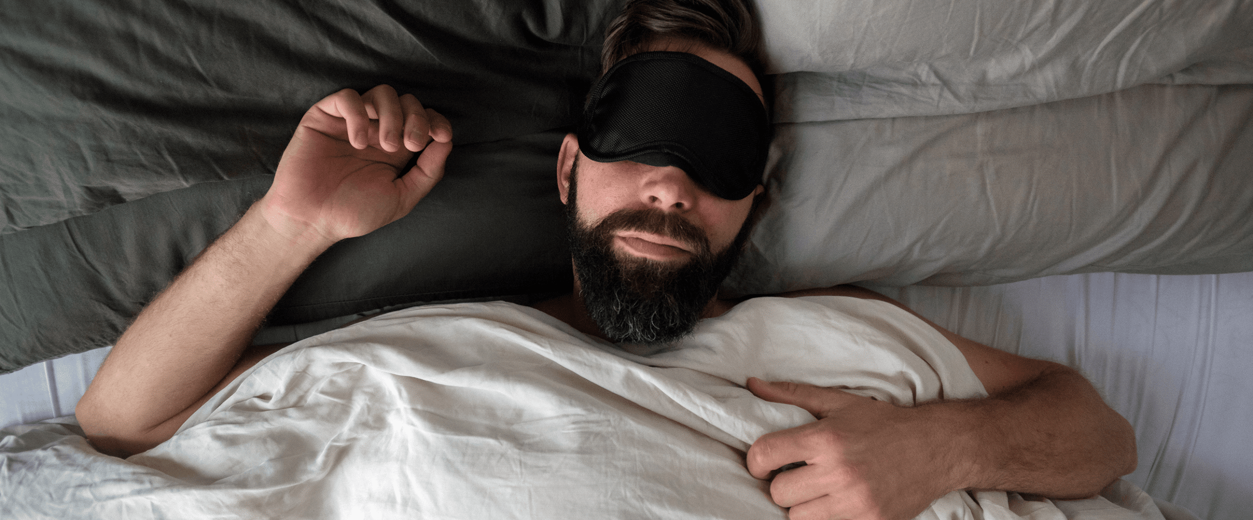 a man sleeps on his back in bed wearing an eye mask