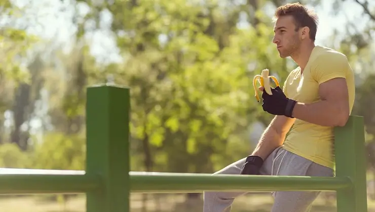 man eating banana and leaning on fence