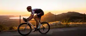 man riding bike on road with mountains in the background