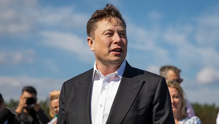 elon musk standing in a crowd of people, his neck scar visible just under the collar of his shirt.
