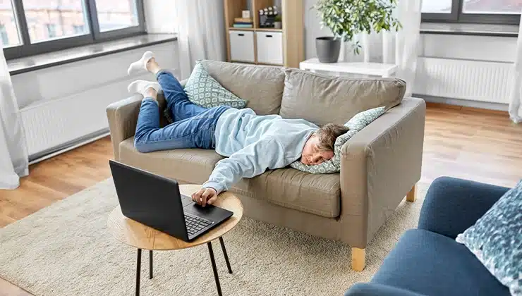 man laying on couch reaching for laptop