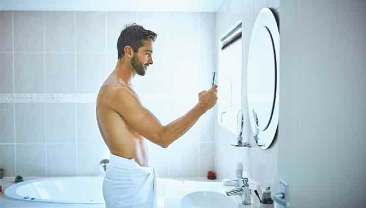 Man taking mirror selfie in bathroom wearing a towel