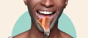 Man smiling while holding a bite of salmon on a fork up to his mouth