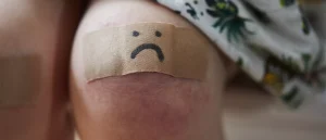 A band-aid grazed knee with a sad face drawn on it
