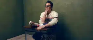 Johnny Knoxville poses for a phone sitting at a desk.