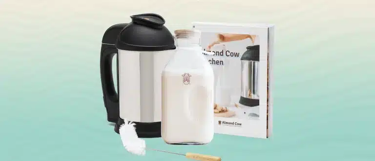 Almond Cow Nut Machine with glass jug, cleaner brush, and recipe book on a blue gradient background