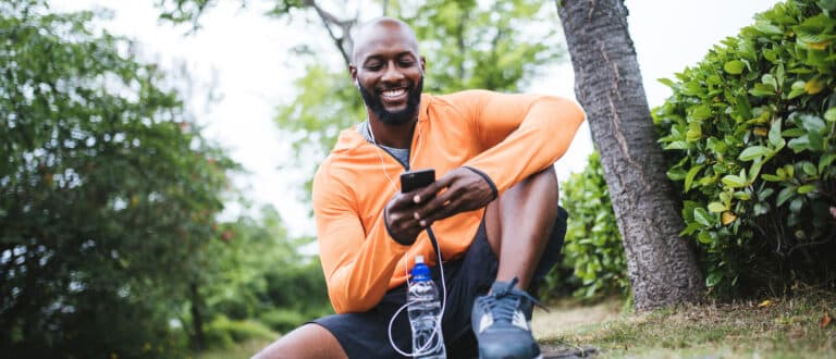Man sitting down after workout lookin gon phone smiling