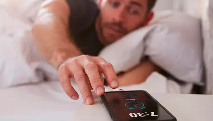 Man reaching for phone on nightstand to turn off alarm