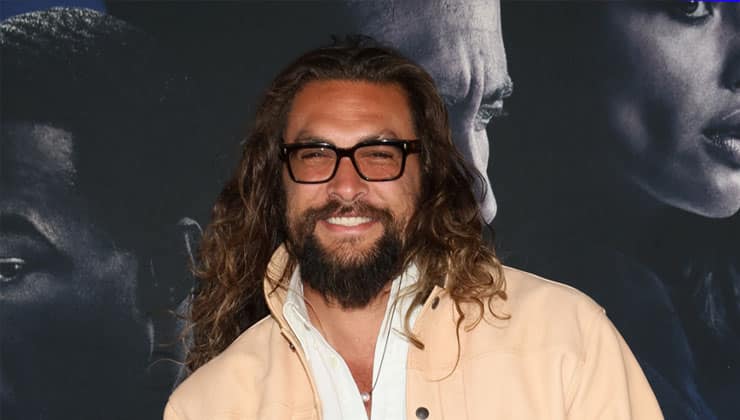 Jason Momoa standing in front of backdrop