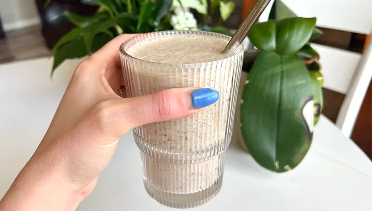 Hand holding a smoothie with a plant in the background
