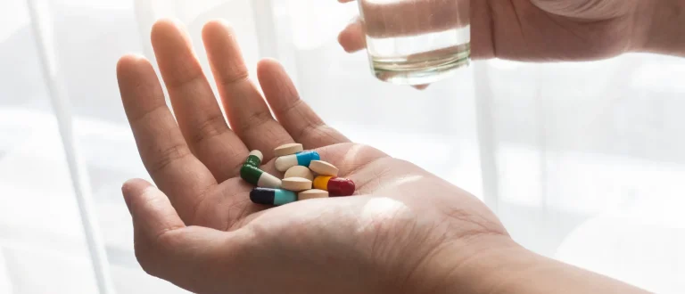man holding a variety of colorful vitamins in one hand, and water in the other.