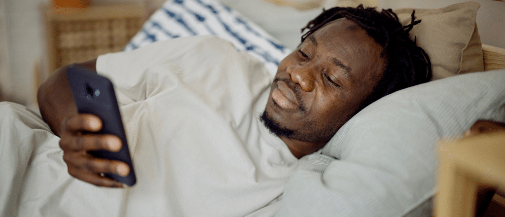 Man lays in bed looking at his smart phone