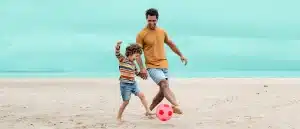 Father and son kicking soccer ball on the beach
