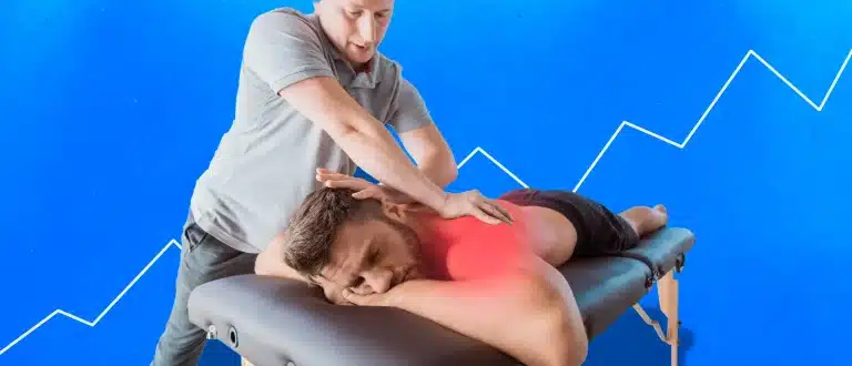 Man laying on a chiropractor table face down with an achy back with a chiropractor standing above him and hands in position to make an adjustment.
