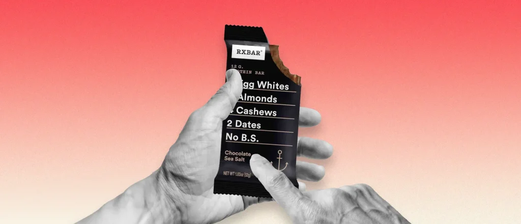 Man holding an RXBar and pointing to the ingredients listed on the front of the label.
