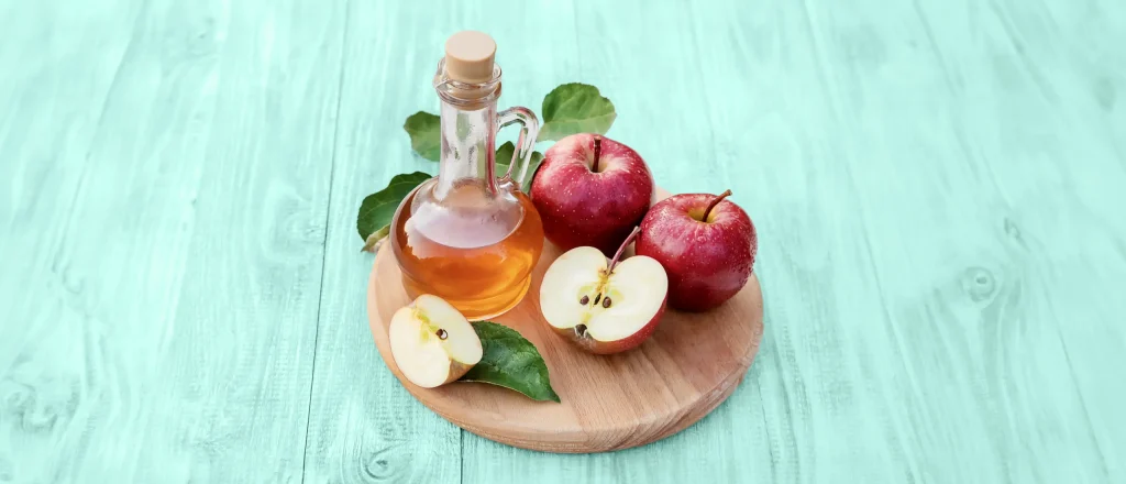 Apple cider vinegar on a wood board with apples