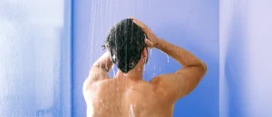man stands in a cold shower and runs his hands through his hair