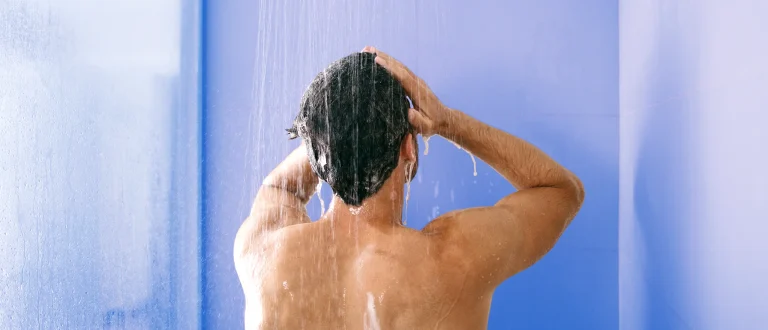 man stands in a cold shower and runs his hands through his hair