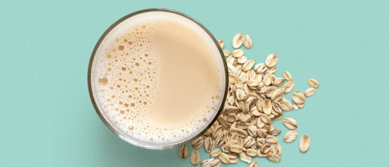Cup of oat milk next to oats on a blue background