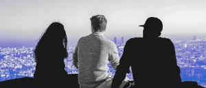3 people sitting on ledge looking over the city with 2 of the people blacked out