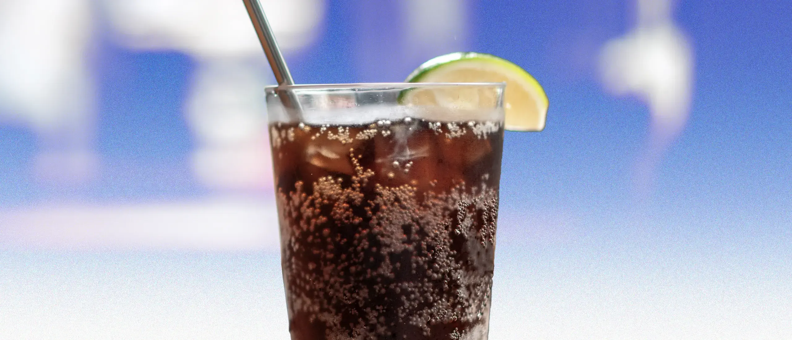 Diet Soda in a cup with a lime and a straw on a blue background.
