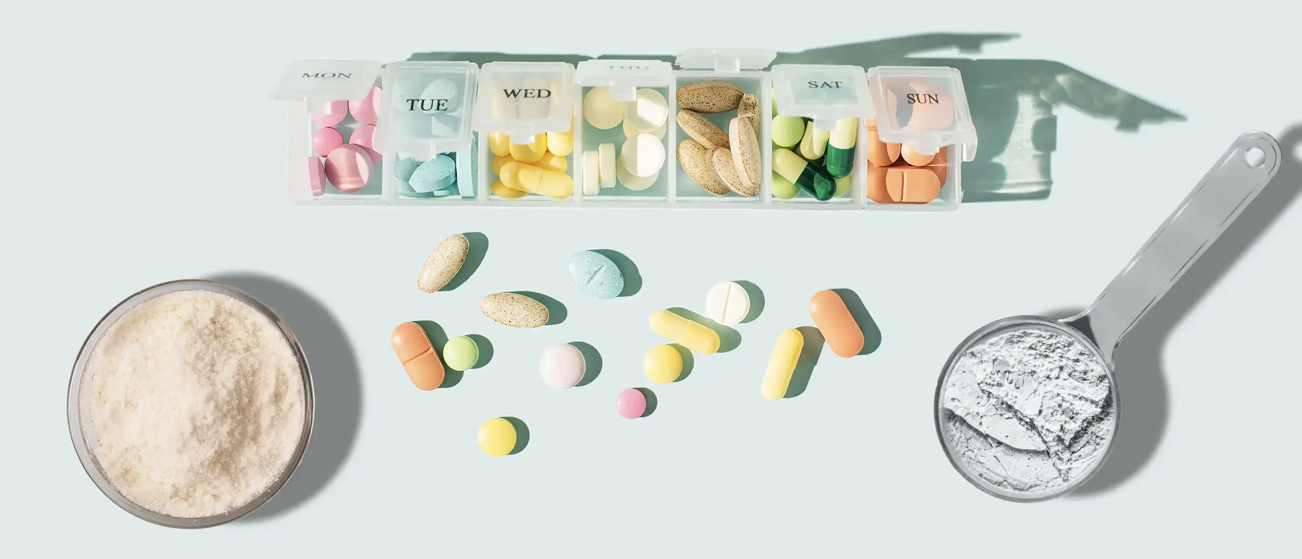 A pill box with colorful pills, a powdered drink, and a scoop of powder.